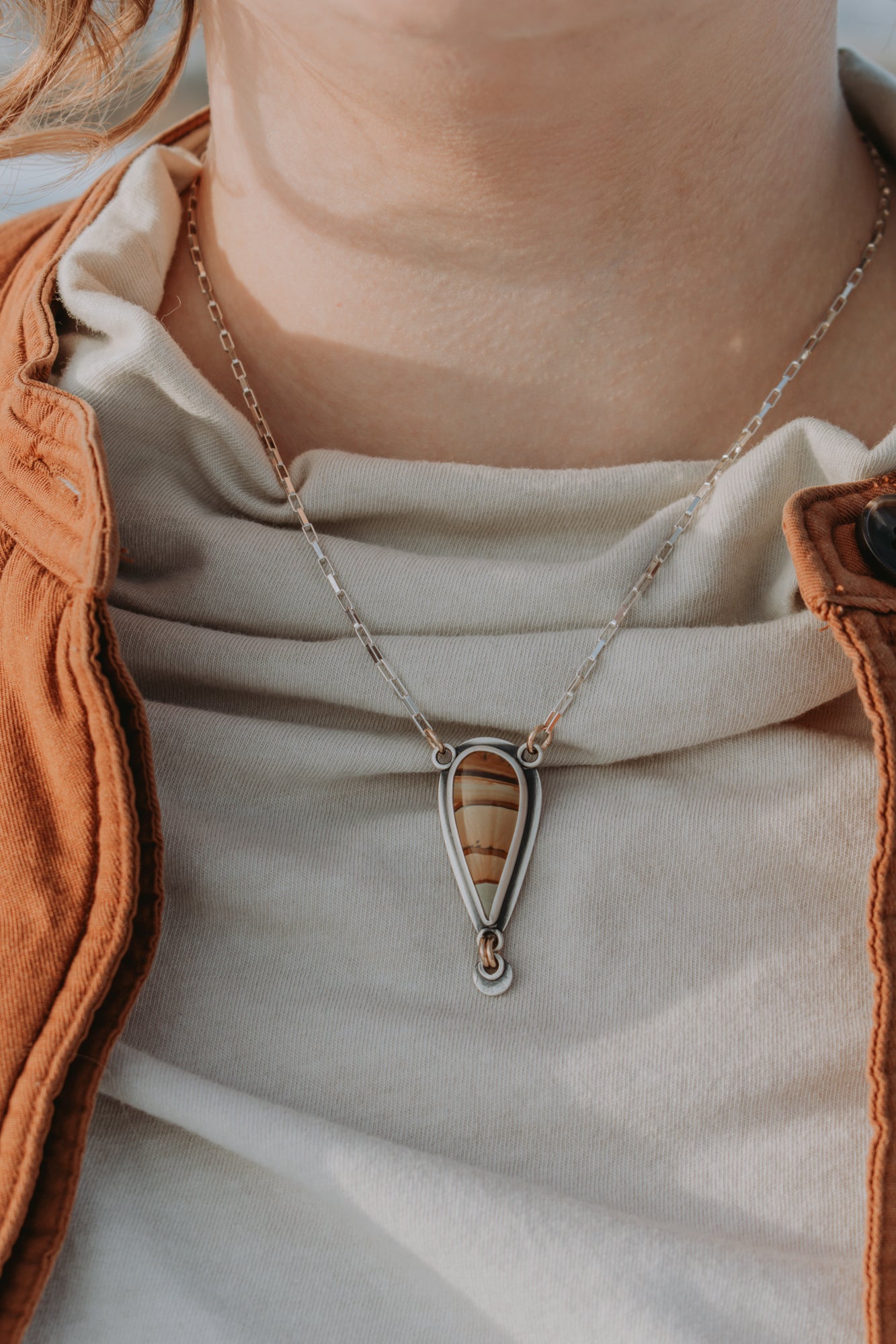 A woman is wearing a white mock-neck shirt with a teardrop shaped Picture Jasper necklace. The image is cropped in tightly to the necklace.