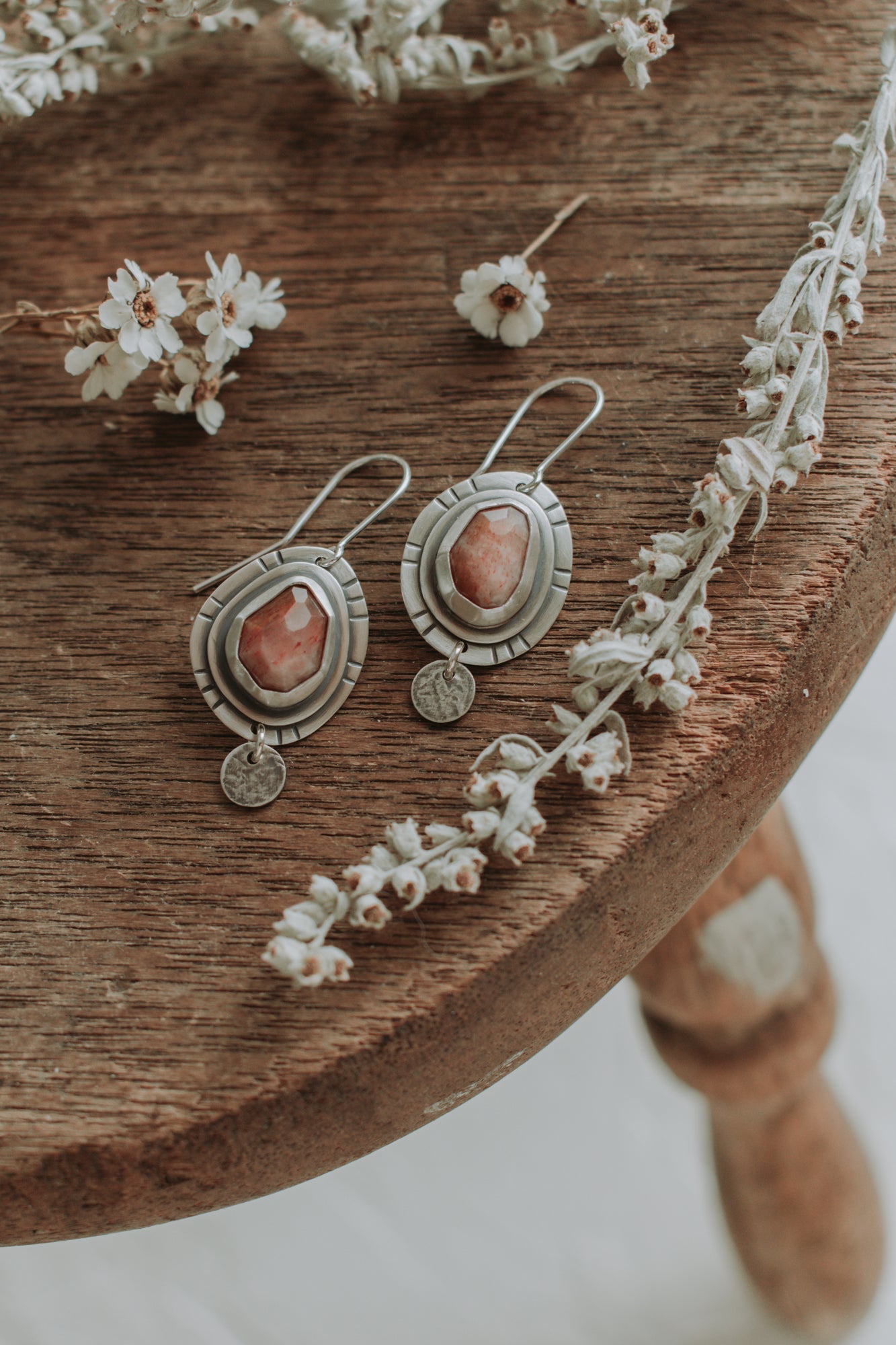 A pair of sterling silver earrings made with faceted pink sunstones sit atop an antique wooden stool. 